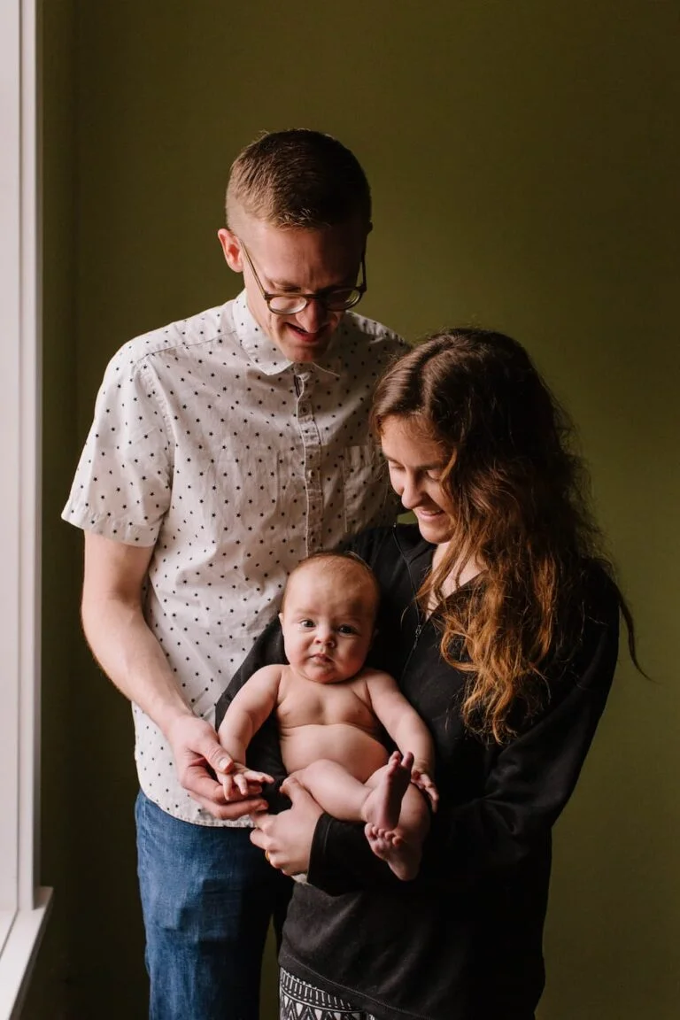 Un homme et une femme tenant un bébé devant une fenêtre.